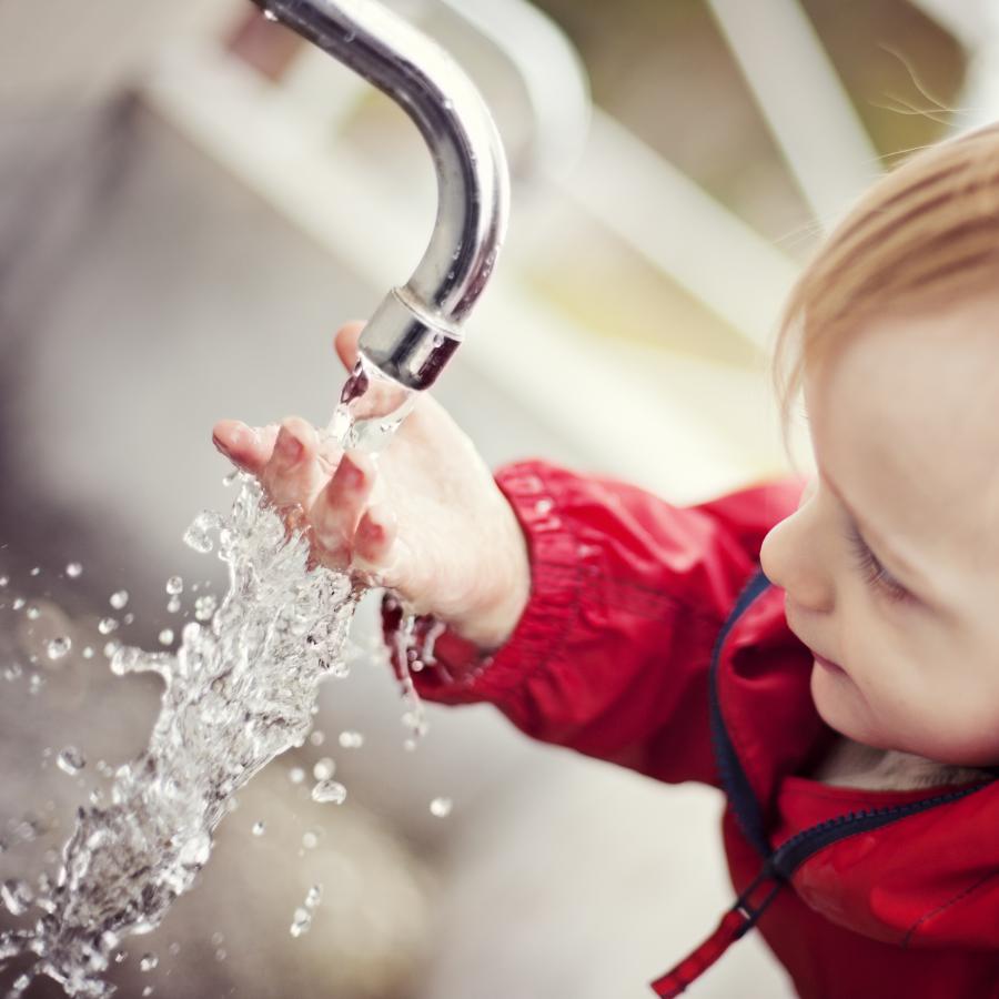 Infant boy washing hands with tap water